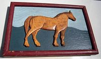 Front view of the carved pine horse in red frame with painted background.