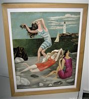 Framed surrealist style art print featuring three women in bathing suits on beach with lighthouse and boat in background.