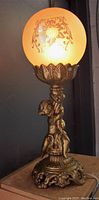 Front view of antique table lamp showing cherub figure and etched glass globe lit up.