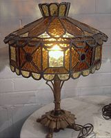 Gothic stained glass table lamp lit photo showing amber and yellow textured glass panels with dark metal base on white surface