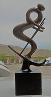 Front-left profile view of the abstract downhill skier statue on podium base, showing the curves and ski poles