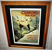 Frontal image of framed Chamonix Mont Blanc ski travel poster showing two skiers mid-air with snowy mountain background in oak frame with black mat.