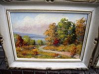 Frontal view of ornately framed pastoral landscape oil painting on canvas signed by A Vlaharek, showing the winding path, trees, and bodies of water in the distant background.