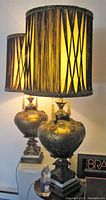 Pair of large table lamps with gilded urn-shaped glass bases and tall cylindrical fringed shades on ornate square metal bases with marble slabs.
