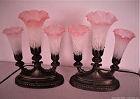 Pair of pink frosted glass three-shade table lamps shown unlit against white background. Each lamp has three fluted glass shades with pink hue and a bronze-toned metal base with decorative detailing.