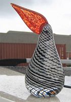 Side view of striped laticino Murano glass bird figurine with elongated orange beak. Shows clear glass with black and white stripes and textured orange beak.