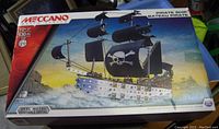 Box front showing the Meccano Pirate Ship Metal Construction Set graphic and details including 630 pieces and recommended age 10+. The design on the box includes the assembled pirate ship with black sails and a skull and crossbones symbol.