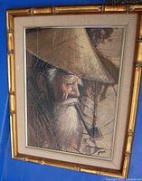 Framed oil painting showing an elderly Asian man with white beard and conical hat, signature visible at bottom right corner. Bamboo style gold frame with beige matting.