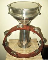 Wooden tambourine with metal jingles placed around the reflective metal tabla drum, showing size comparison and condition.