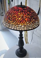 Lamp in ambient light showing dome shaped pebble glass shade with warm tones and dark metal ornate base.