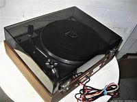 Side angle showing dark tinted dust cover, wood base, and cables coiled beside the unit.