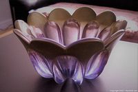 Purple scalloped edge art glass bowl with translucent, iridescent finish photographed from side angle showing shape and color gradient.