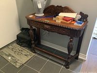 Front view of antique console table showing detailed carved wooden apron, drawer with lion head pull, turned legs, and wooden top with assorted items