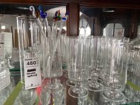Clear highball glasses arranged in two rows, along with art glass stir sticks with colorful decorative tops in a small glass container.