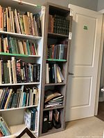 Tall narrow bookcase against a wall, filled with various books only for staging, not included.