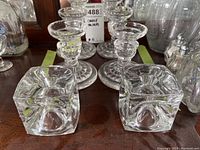 Four glass candle holders on a wooden surface with labels behind them.