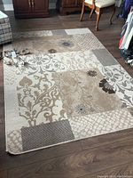 Full view of abstract floral pattern area rug on wood floor with patterned design and neutral tones.