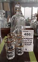 Photo of the decanter with stopper and eight small glasses in front, with a label showing the lot number and description.