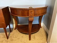 Front view of wooden demilune table showing carved medallion detail on apron, pineapple carving on leg and lower shelf.