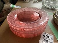 Stack of eight cranberry colored pressed glass plates with visible etched floral and scroll design on edges.