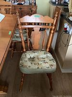 Front view of a maple dining chair with cushioned seat, showing turned spindle backrest and legs with floral and vintage themed cushion fabric.