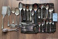 Full assortment of vintage plated serveware pieces arranged on dark fabric displaying wear and tarnish.