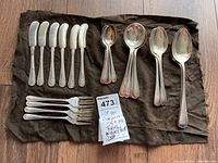 Full set of 25+ pieces of Birks Regency plated flatware including butter knives, forks, teaspoons, tablespoons, and a serving spoon laid on a black cloth.