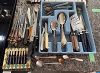 Photo of multiple vintage flatware items arranged in plastic trays and boxes including knives, forks, spoons, fondue forks, spatulas and steak cutters.
