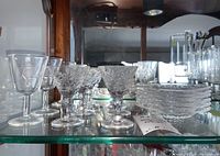 Photo of clear etched glass stemware goblets and a stack of small clear glass plates