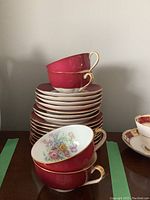 Stacked tea cups, saucers and side plates showing pink and floral pattern with gold trim