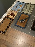 Four welcome mats and one boot tray showing their colors and designs on tiled floor.