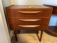 Frontal view of wooden mid-century modern nightstand with three drawers and angular wood pulls