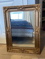 Full front view of the mirror standing upright, showing decorative gold-tone frame with visible wear and chips.