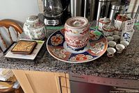 Overall view of the oriental china ware set on kitchen counter including ginger jars, sake set, trivet, coasters, and decorative plate.
