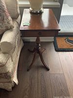 Side view of the wood pedestal side table showing single drawer and brass foot caps.