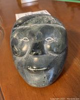 Frontal view of signed soapstone face sculpture showing carved eyes, nose, and mouth details.