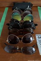 Photo showing seven pairs of sunglasses laid out in a row on a wooden surface including one with bifocal lenses