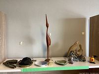 Full display of the lot items including teak crane, brass dish, Wedgwood dish, Royal Copenhagen dish, bird figurines, leather pouch, metal tools, and small ceramic dog figurine.