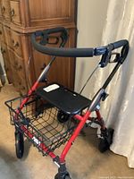 Front view showing four wheels, wire basket, black plastic seat on red walker frame