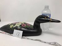 Side angle of the black wooden Art Deco loon figurine, showing floral detailing and scale with measuring tape and water bottle.