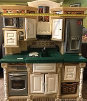 Front view of plastic child's play kitchen showing microwave, oven, sink, stove, refrigerator, and cabinets.