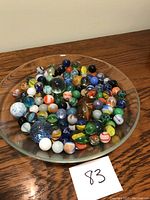 Full view of 83 assorted marbles in a glass dish on wooden surface