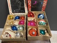 Two open boxes of assorted vintage glass Christmas ornaments in various colors and decorative patterns.
