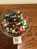 Overhead photo showing a clear dish filled with a variety of colored marbles of assorted sizes on a wooden surface.