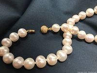 Close-up image of the pearl necklace showing the gold-tone spherical clasp and the size and shape of the pearls.