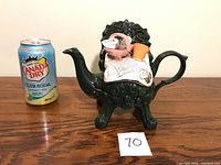 Full shot showing the entire ceramic tea pot shaped as a dark green ornate chair next to a soda can for scale.