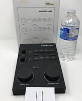 Front view of Propellerhead Balance audio interface next to water bottle and manual, shows knobs and buttons.