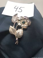 Front-angle photo of the vintage sterling silver flower brooch showing the single flower and three detailed leaves with a green sapphire in the center.