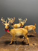 Photo showing three vintage plastic reindeer figurines with tan bodies, white underbellies, antlers, and wreath collars with red bows.