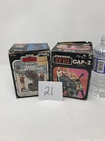 Front view of two vintage Star Wars Kenner toy boxes: Radar Laser Cannon and CAP-2 Captivator, next to a water bottle for scale. Boxes are visibly worn and damaged.